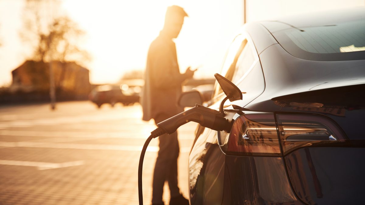 Waiting for the automobile to charge. Man is standing near his electric car outdoors.