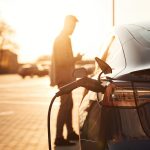 Waiting for the automobile to charge. Man is standing near his electric car outdoors.