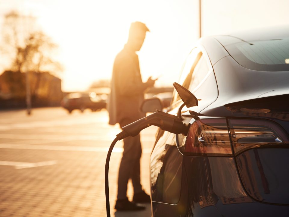 Waiting for the automobile to charge. Man is standing near his electric car outdoors.